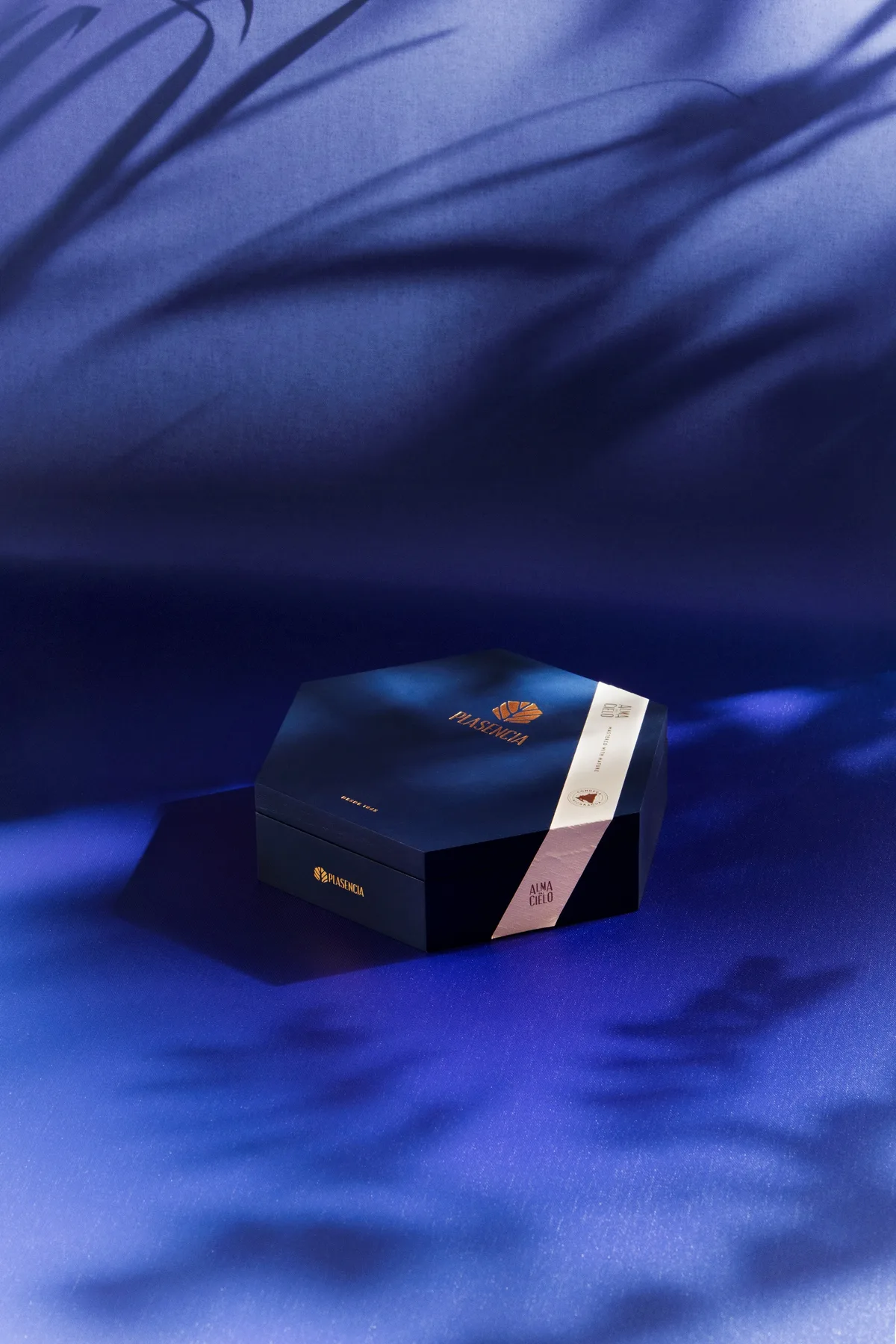 A closed box of Alma del Cielo on blue cloth, leaf shadows across it
