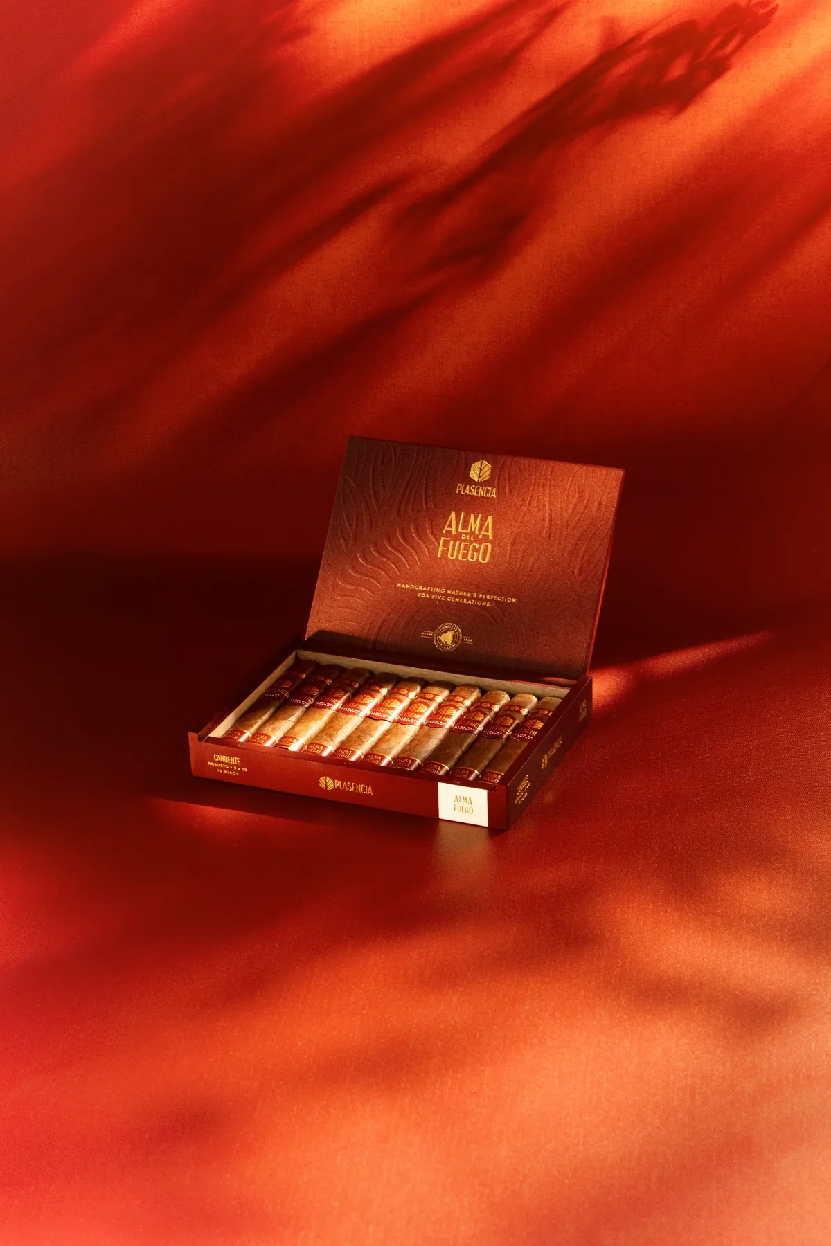 An open box of Alma del Fuego on red cloth, leaf shadows across it