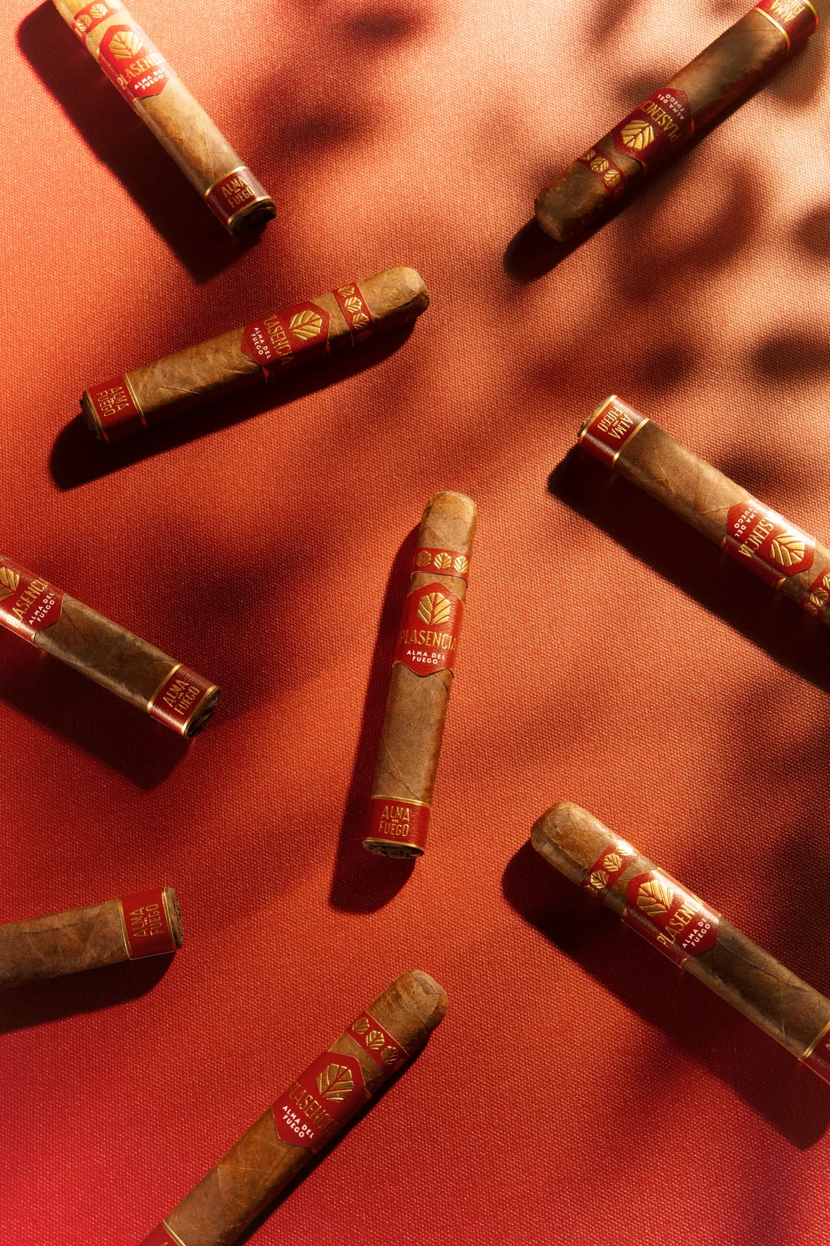 Alma del Fuego cigars on red cloth, leaf shadows across them