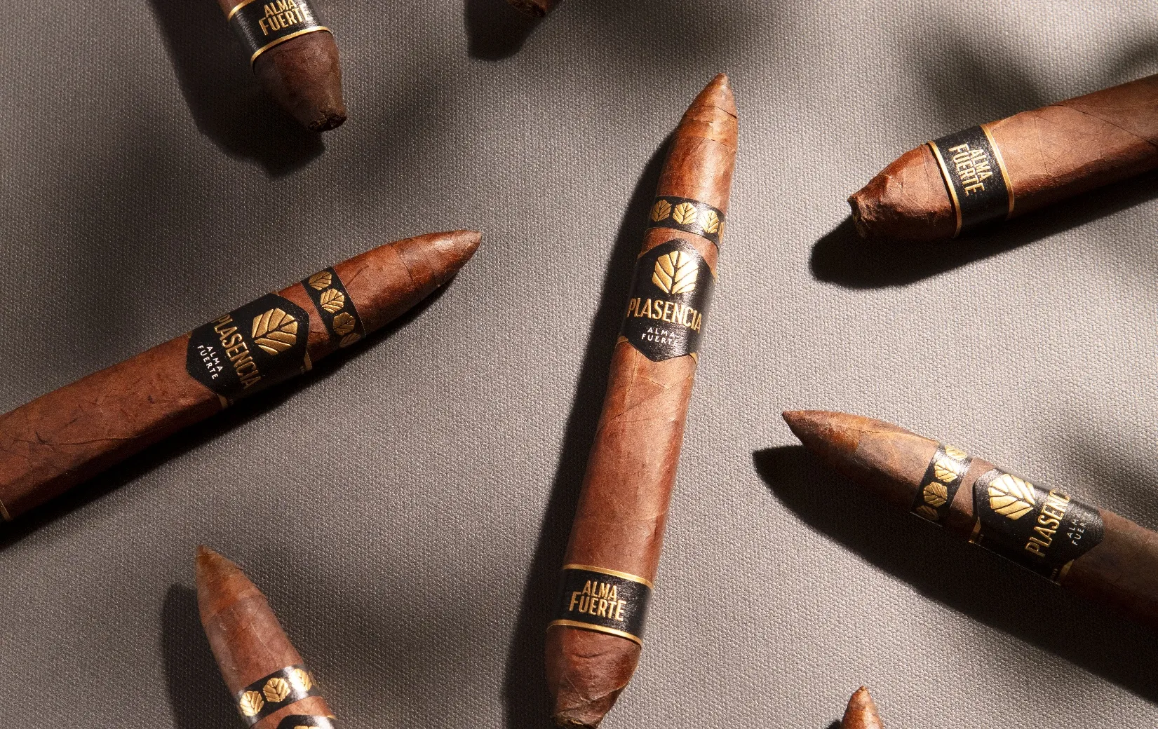 Alma Fuerte cigars laid out on cloth, a leaf shadow across them