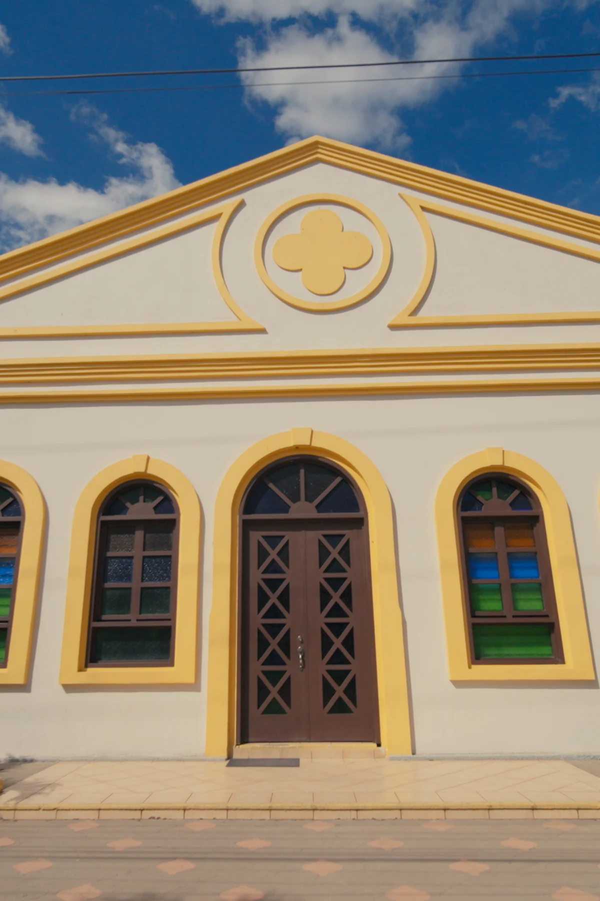 A colonial building with a yellow trimmed facade and arched windows under a blue sky
