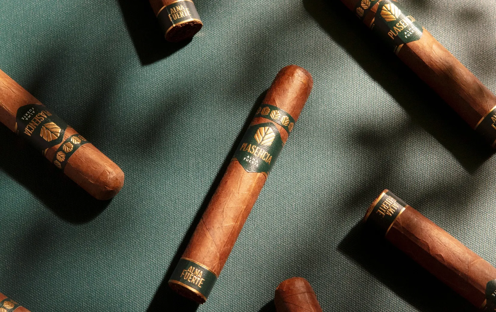 Alma Fuerte cigars on green cloth, leaf shadows across them