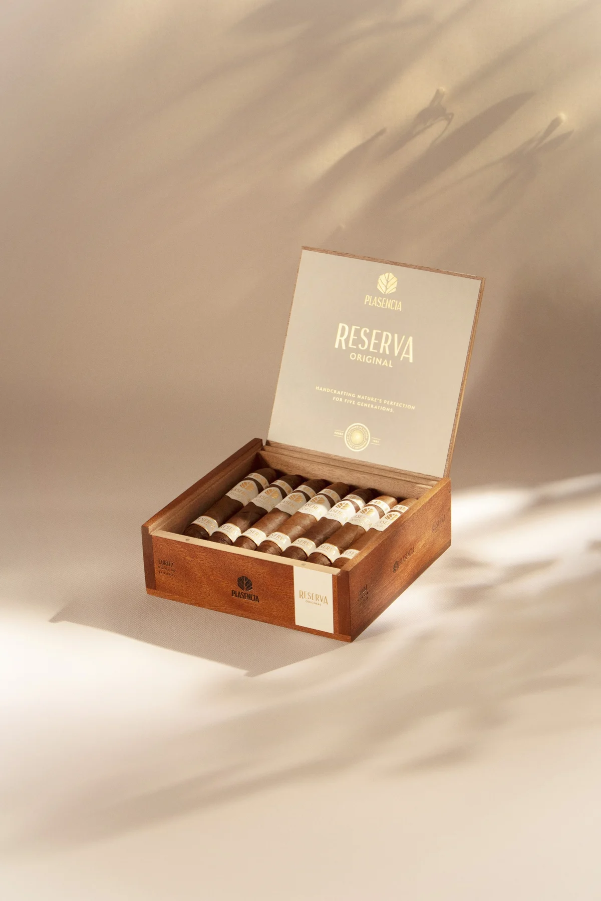 An open box of Reserva Original on warm sand, palm shadows across it
